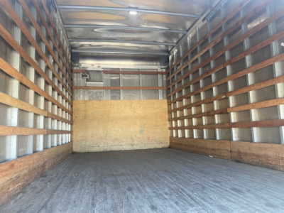 Truck box interior showing metal walls with wooden slats and a plywood bulkhead at the far end.