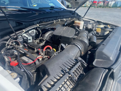 Ford F-550 engine bay showing air intake, battery, and various hoses under the hood.