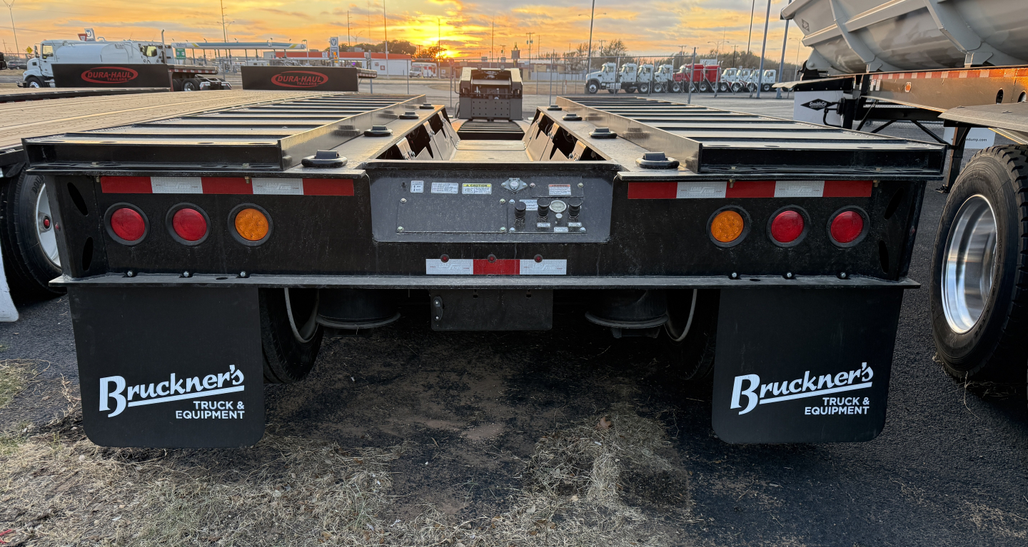 Trailer rear view showing Load King equipment trailer with mudflaps reading Buckner's Truck & Equipment and taillights, black frame, license plate area, and reflectors.