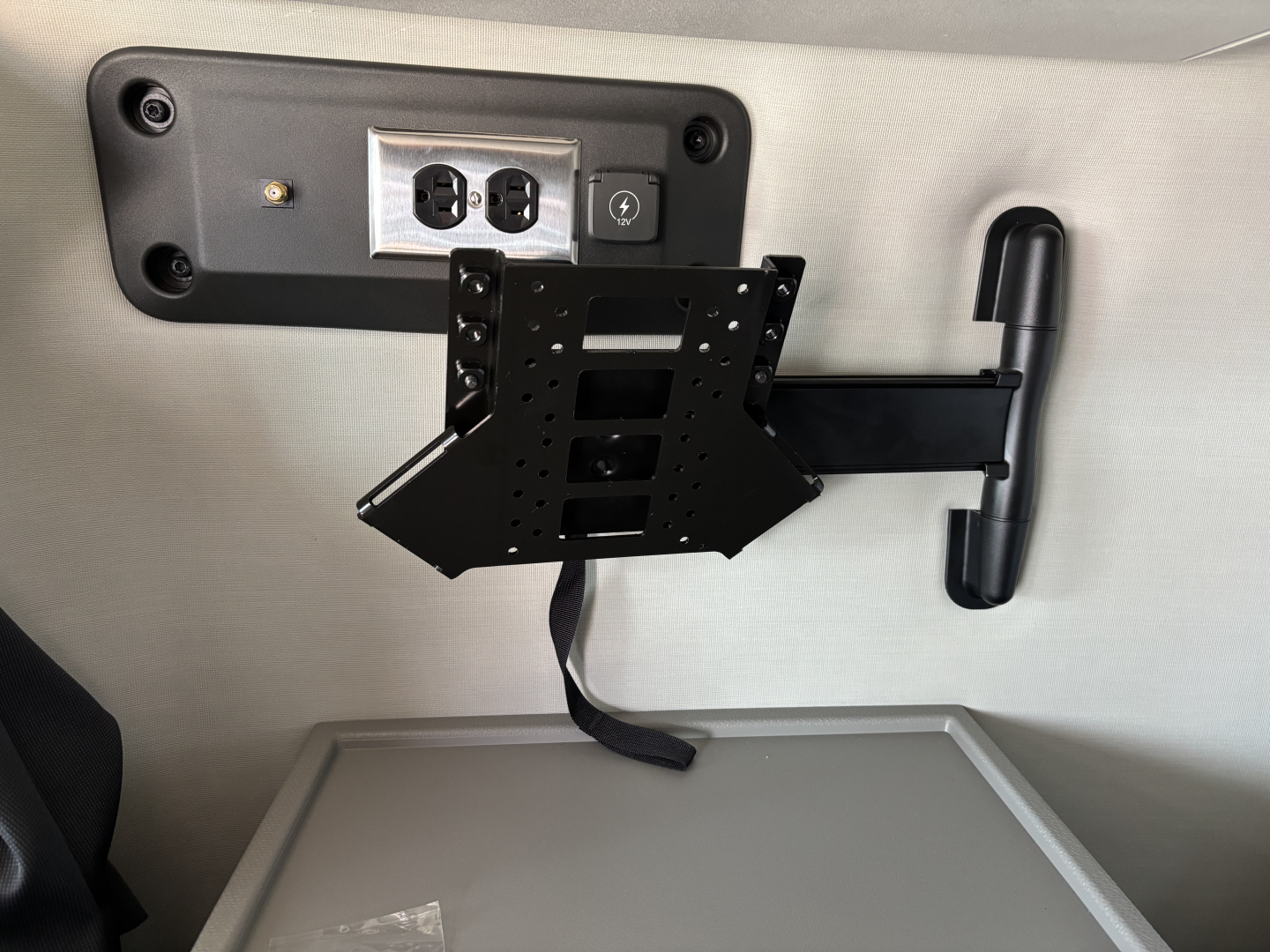 Interior cab area showing adjustable monitor/bracket mount and power outlet panel on Volvo trucks sleeper cab, wall texture light, black metal bracket with multiple holes.