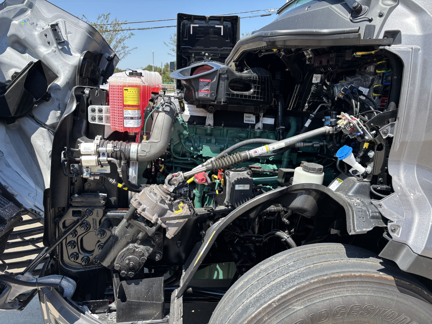 Volvo VNL truck engine bay with exposed components and open hood showing green engine block and various hoses and cables.