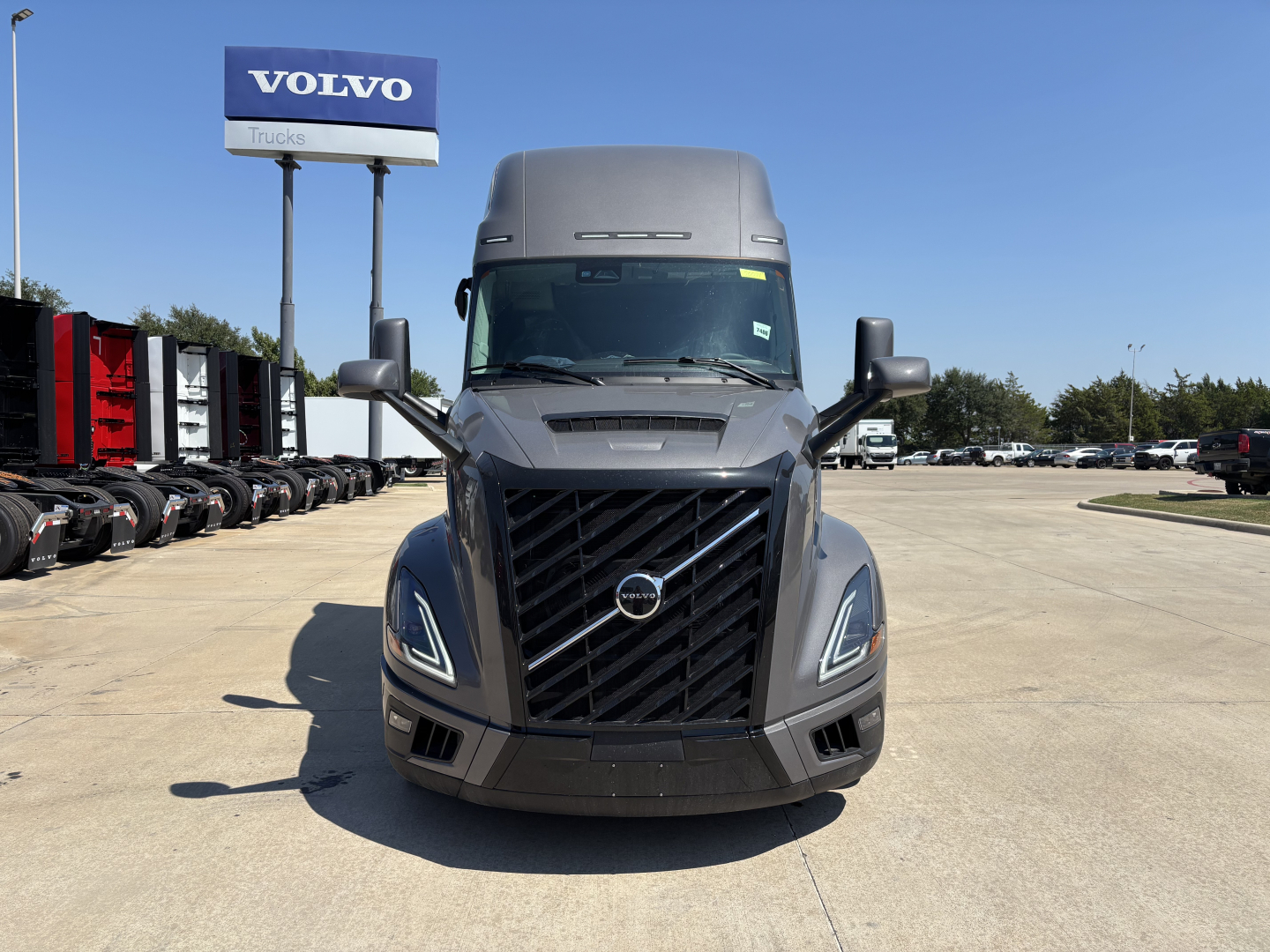 Front view of a new 2026 Volvo VNL64T860 tractor in a dealership lot with a Volvo Trucks sign in background.