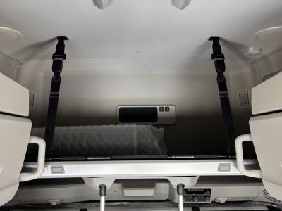 Interior of a Volvo VNL64T860 cab showing bunk area with folded bed, storage shelf, and shoulder-height straps.
