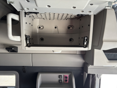 Open overhead storage compartment in Volvo VNL64T860 cab showing interior hinges and mounting points.