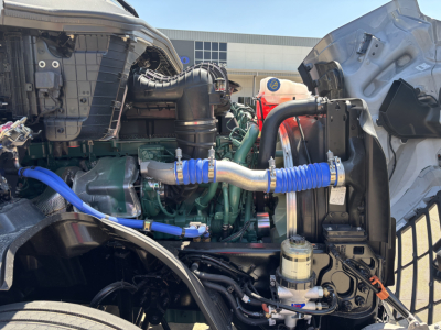 Volvo VNL64T860 engine bay view with blue hoses and intake piping, visible coolant reservoir, and various engine components.