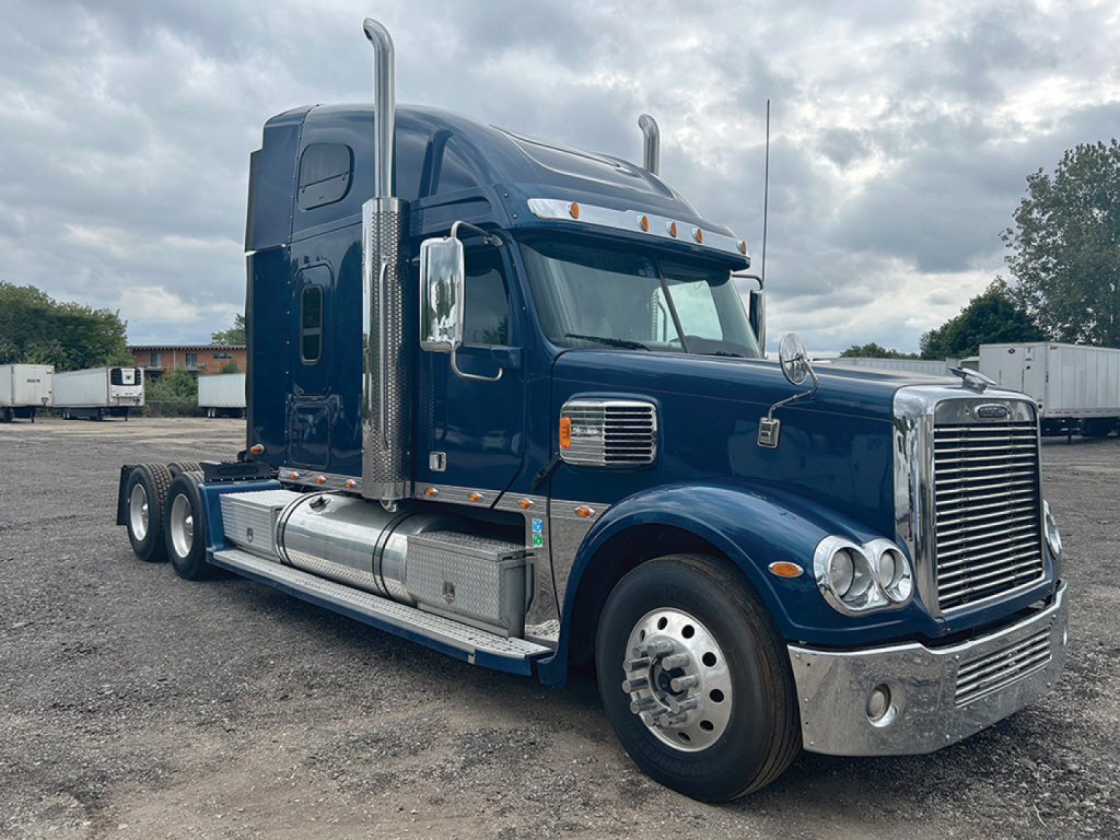 Freightliner Coronado heavy-duty truck in blue, side view showing chrome grille, exhaust stacks, and sleeper cab.