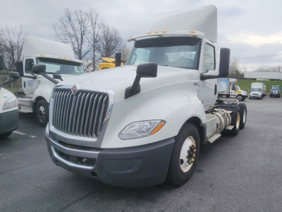 Truck cab showing International LT625 in white with grille, side mirrors, and front bumper; sleeper cab over; multiple trucks in background.