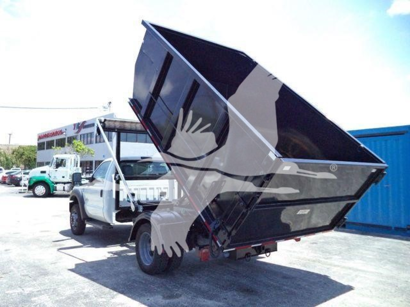 Truck with a raised black dump bed on a Ford F-550 chassis in a lot.