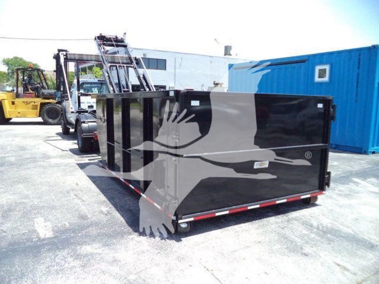 Rolloff container in a truck yard showing a large black rectangular dumpster with red and white reflective striping along the base.