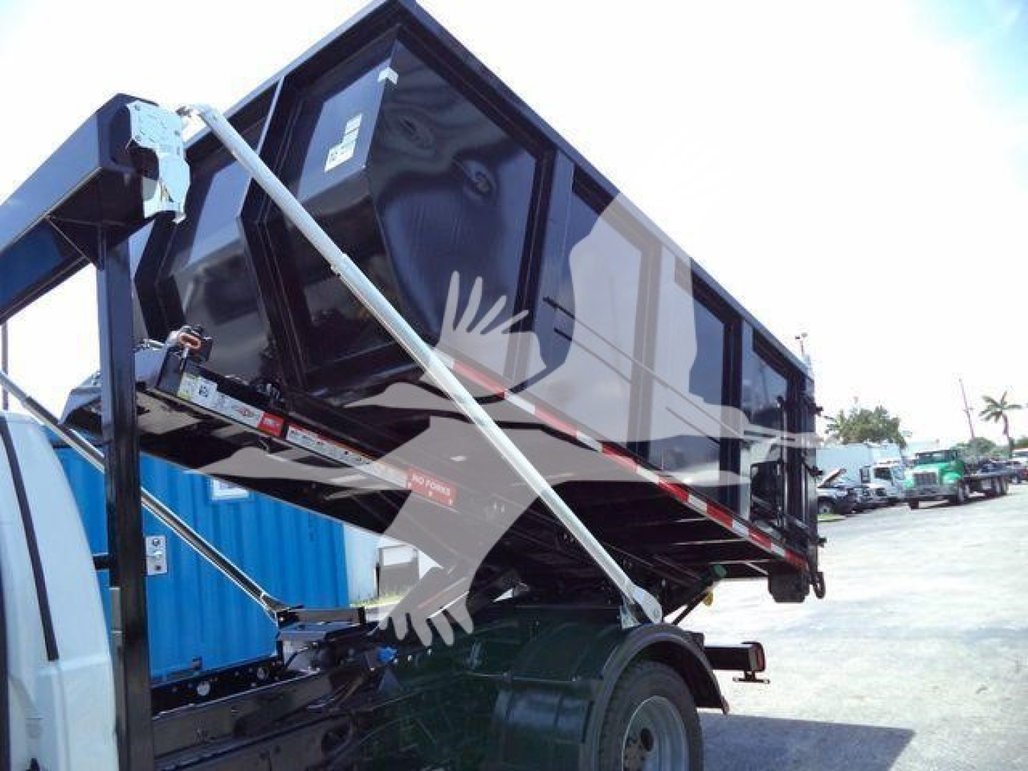 Ford F-550 roll-off truck bed raised on hydraulic arms with black cargo container.