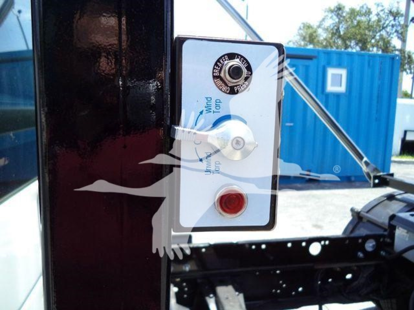 Control panel on a roll-off truck featuring a white rectangular switch panel with a black border, a keyhole and a red push button. The panel shows blue text and a circular lock label.
