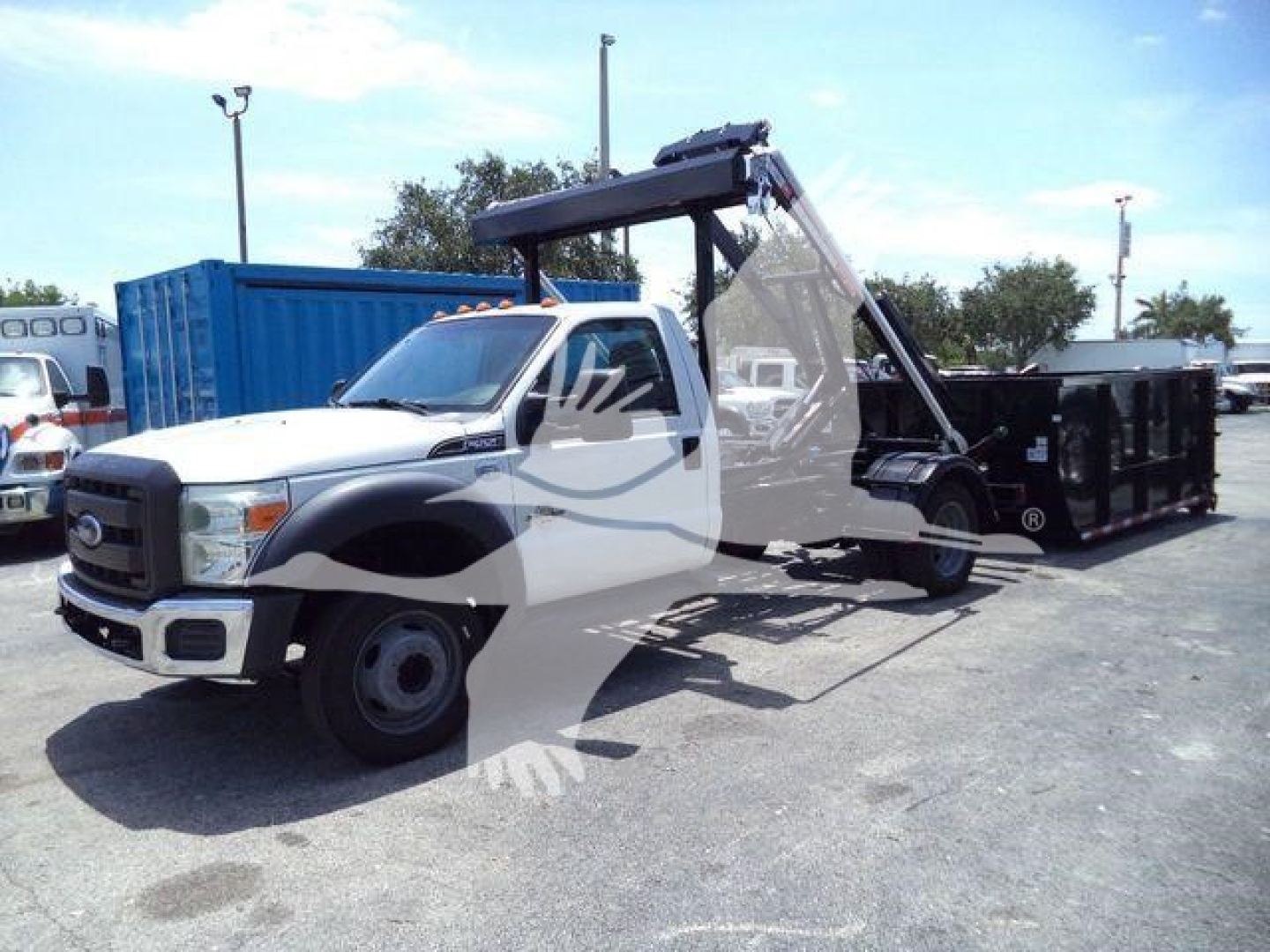 2016 Ford F550 roll-off truck with a hydraulic arm and dumpster body, shown parked with a blue container in background.