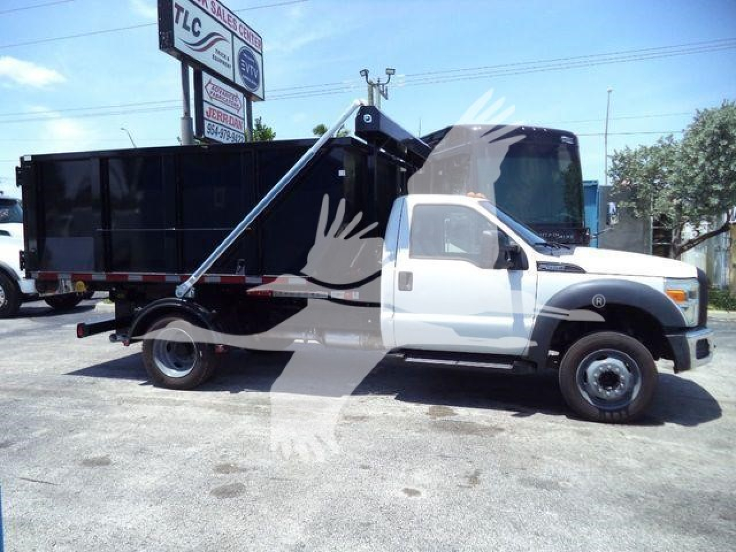 Ford F550 roll-off truck in white and black with a large black dumpster body, side graphics, and extended hydraulic arm.
