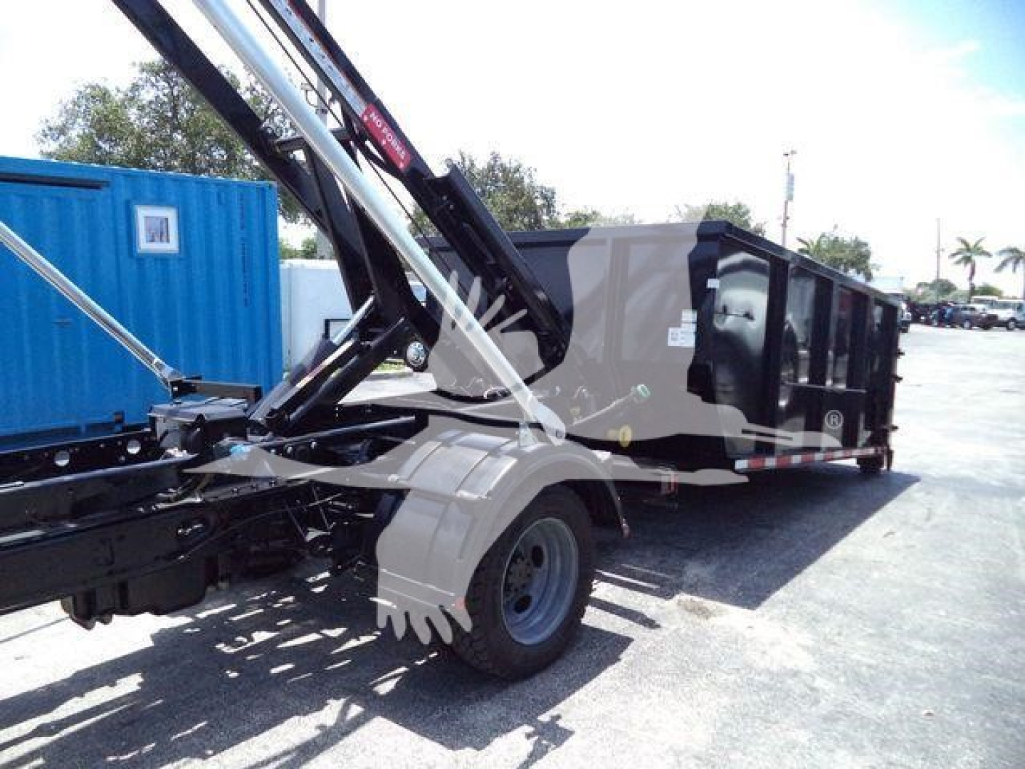 Ford F-550 roll-off truck chassis with hydraulic crane arm and dumping trailer in service view showing wheel and hydraulic components.