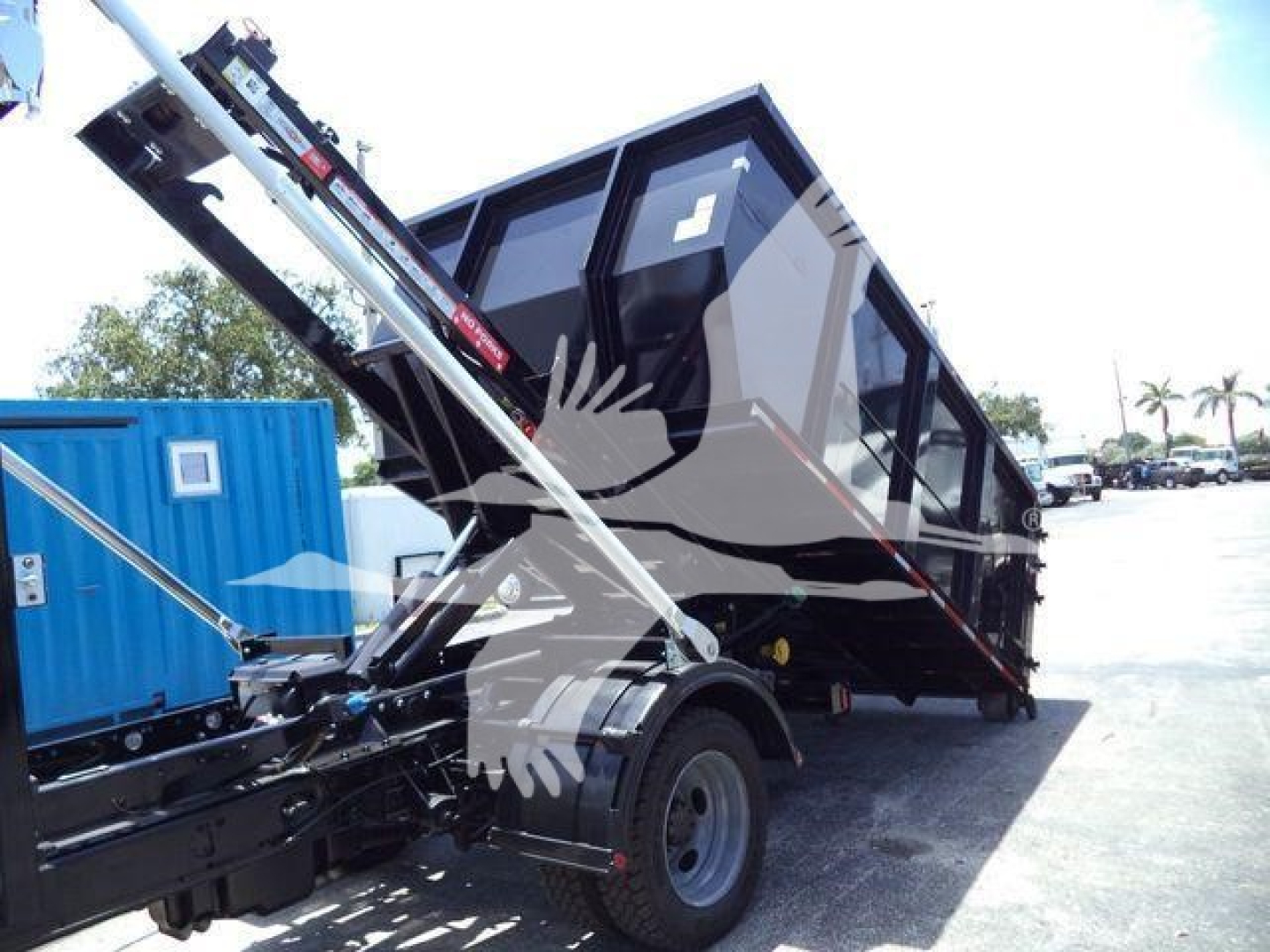 2016 Ford F550 rolloff truck in service showing dumping bed and hydraulic arms, side view with blue portable unit in background.