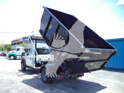 Truck with a raised black dump bed on a Ford F-550 chassis in a lot.