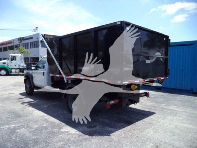 F550 truck with a black roll-off container mounted on a white cab; side and rear view showing the roll-off bed and lift arms.