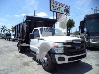 Ford F-550 dump truck roll-off body showing front view and side container in a dealership lot.