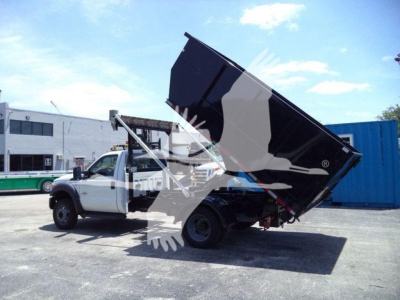 Ford F-550 rollback truck with dumping bed raised, white cab and black bed, in a lot.