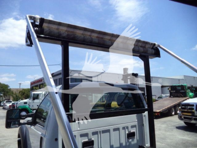 Ford F550 roll-off truck cab with hydraulic hoist structure visible in rear window area and a clear blue sky.