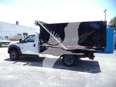Ford F-550 roll-off truck side view showing black dump body with white cab and side graphic.
