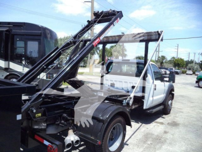 Truck with a roll-off hoist in folded position, white cab, black hydraulic boom arms, viewed from the driver's side rear.
