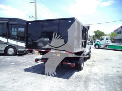 Truck bed showing cargo dump/rolloff box on Ford F-550 rear view with dual wheels and hitch, black/gray box, signage not legible.