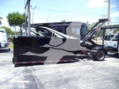 Ford F550 roll-off truck side view showing large black dump bed with crane arm and hydraulic components.
