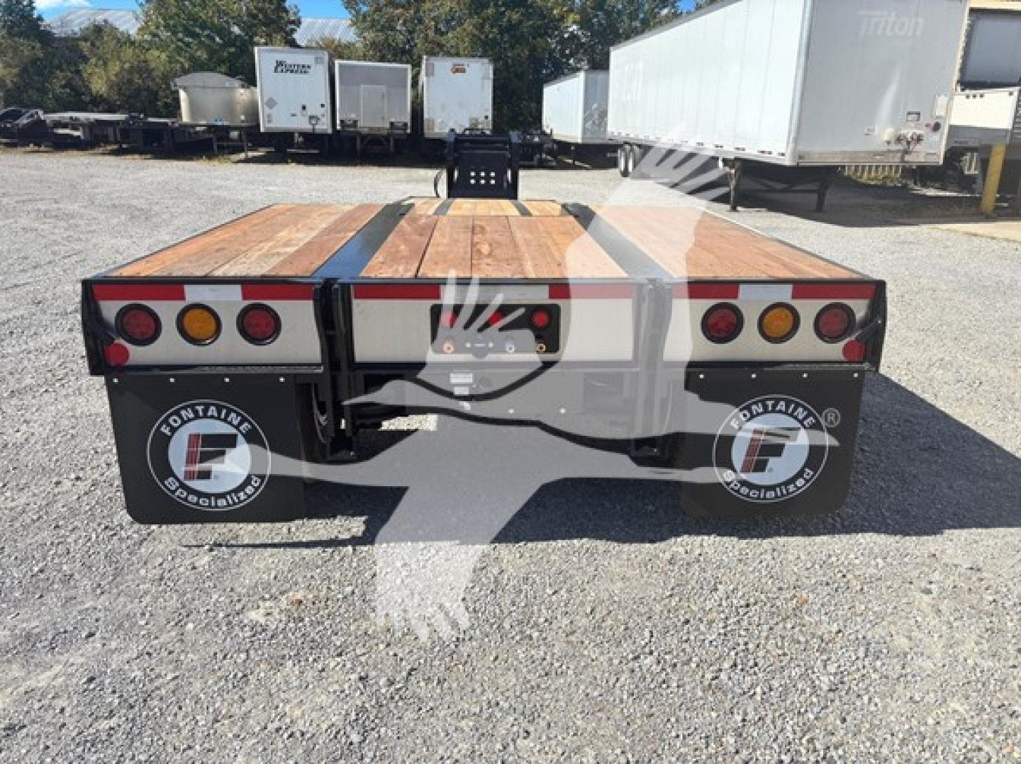 Flatbed trailer rear view showing wooden deck, taillights, and Fontaine logo mud flaps with dual wheels.