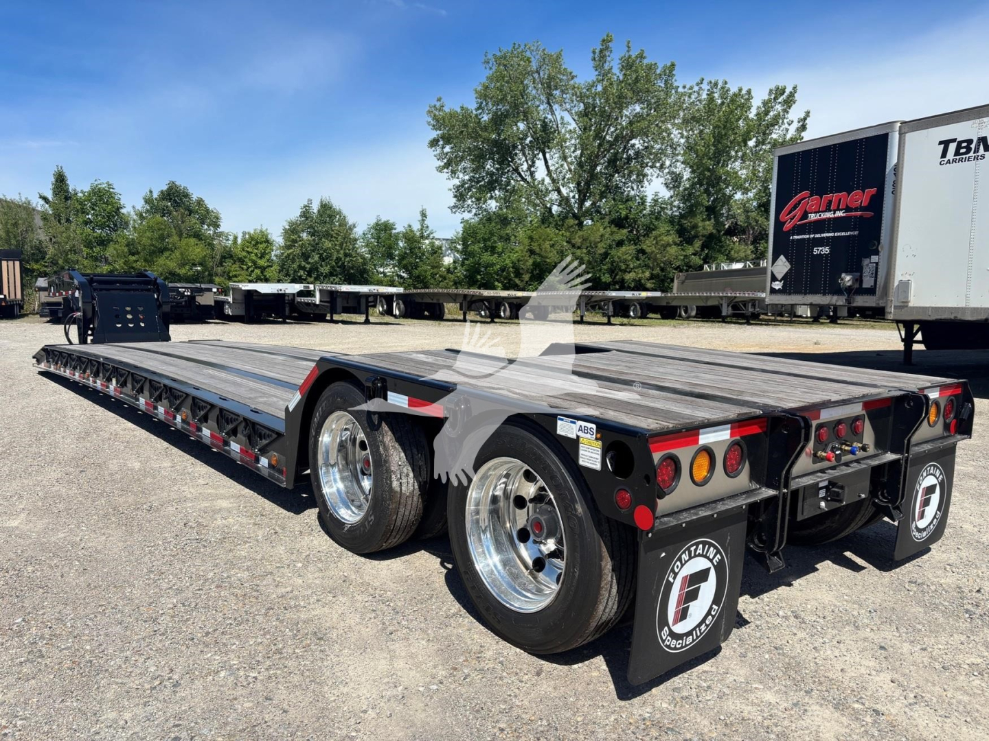 Fontaine Renegade lowboy trailer showing long flatbed with dual rear axles, black mud flaps with Fontaine logo, and chrome wheels.