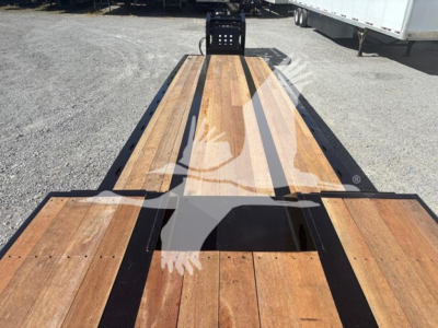 Lowboy trailer bed with wooden deck and black steel frame, viewed from rear toward cab area, showing long flatbed surface.