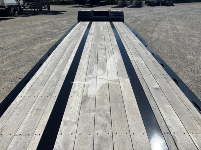 Flatbed trailer deck with wooden planks and black steel rub rails, view from front with gooseneck area in distance