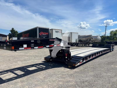  Fontaine Renegade lowboy trailer in a parking lot showing long flatbed with low deck and gooseneck; rear section visible with tandem axles and loading ramps.
