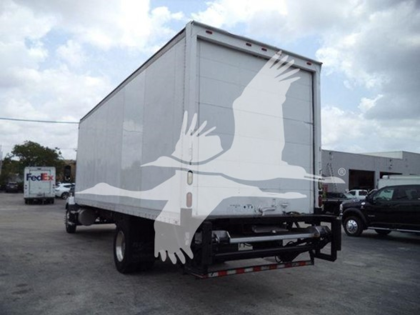 Box truck rear view showing large bird silhouette artwork on back doors and closed trailer with FedEx truck in background