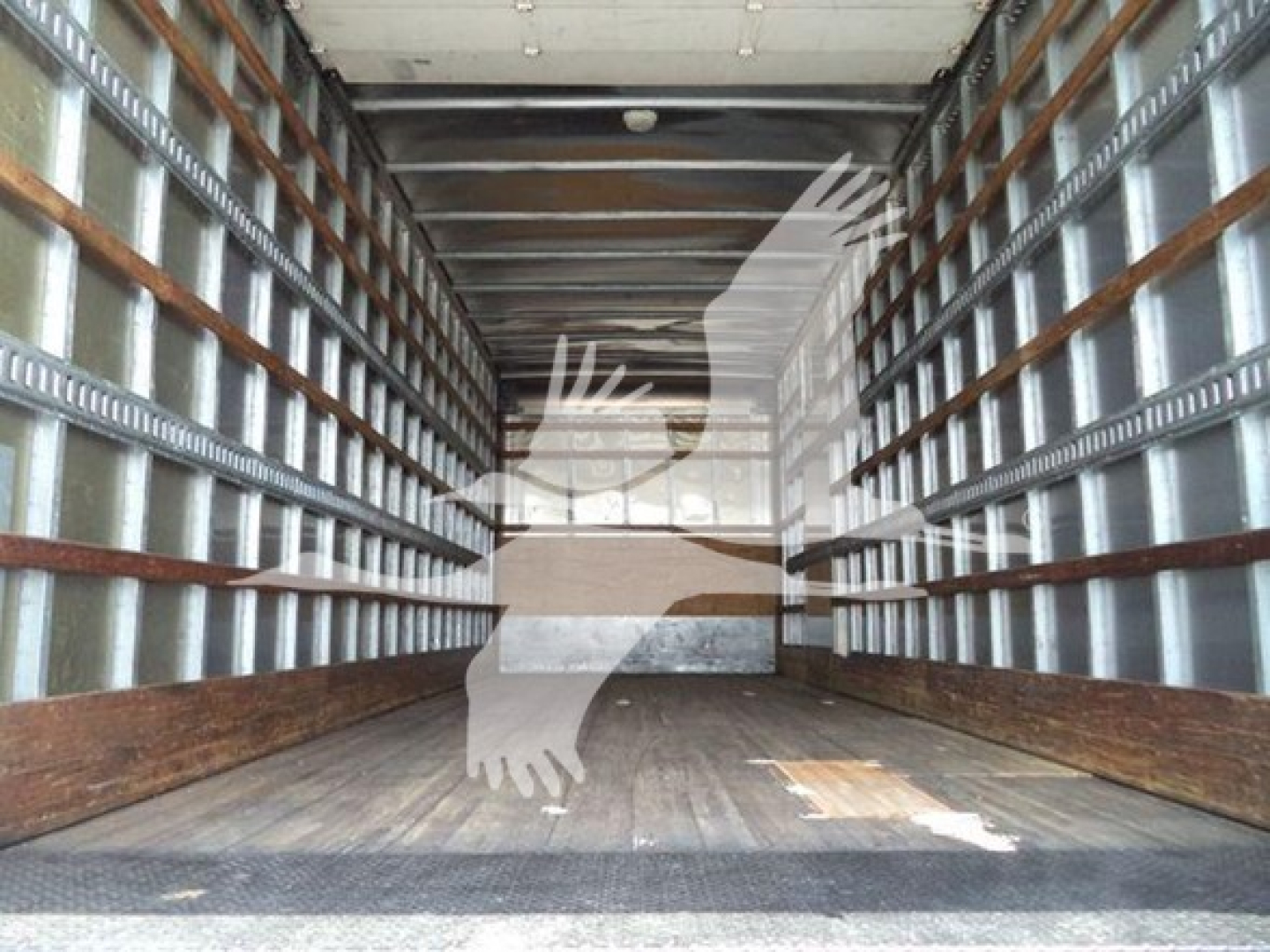 Truck trailer interior with metal side rails and wooden floor, view toward cab door at far end. Overlay silhouette of a bird logo.