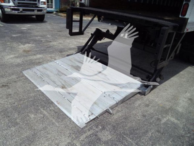 Truck liftgate in lowered position showing metal platform and hydraulic arms at rear of a Mack MD7 box truck.