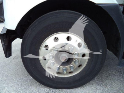 Front wheel of a Mack MD7 truck showing a steel rim with multiple lugnuts and a black tire; faint watermark of birds logo overlain on tire.