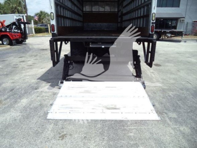 Truck back showing a lowered hydraulic liftgate in a Mack MD7, white ramp extended, open cargo area, concrete ground.