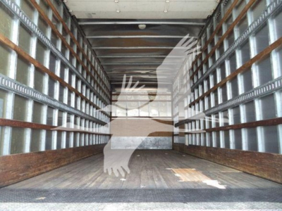Truck trailer interior with metal side rails and wooden floor, view toward cab door at far end. Overlay silhouette of a bird logo.