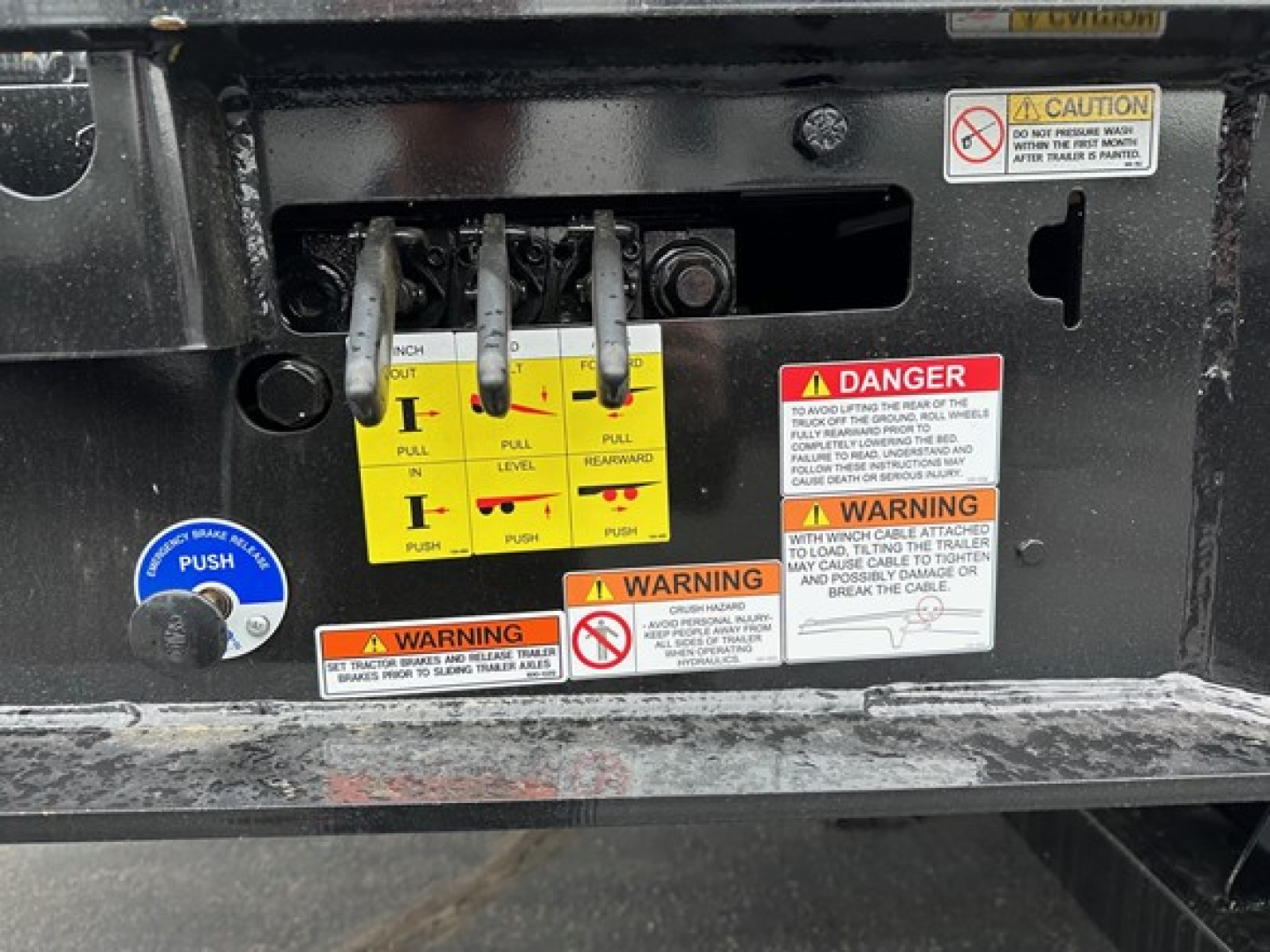 Trailer hitch area with yellow hydraulic lever assembly and multiple warning labels on a Trail-Eze TE801 trailer.