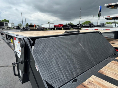 Flatbed trailer with diamond plate toolbox lid open showing wooden deck and storage area; Trail-Eze logo not visible; trailer in lot with other trailers in background.