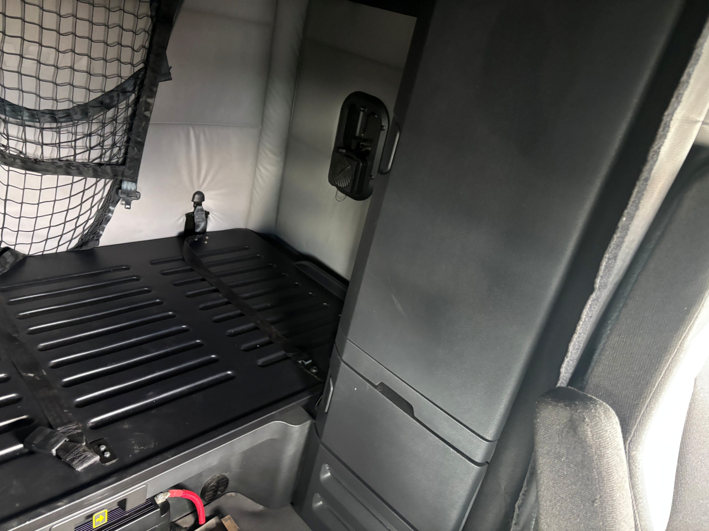 Partial Freightliner CA-126 sleeper cab interior with cargo bed and strap net; glimpse of side panel and rear storage area.