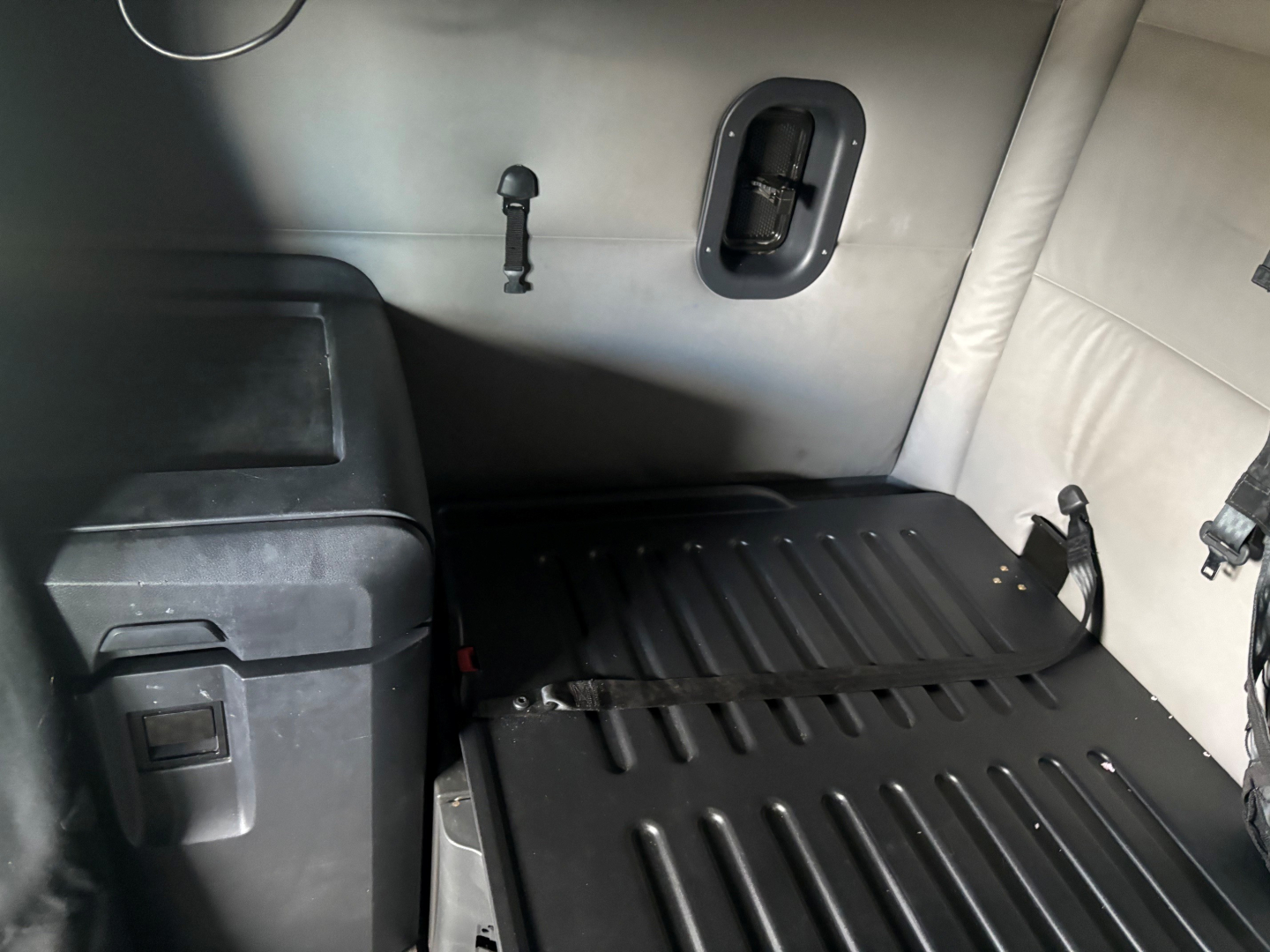 Cab interior showing sleeper area with ribbed rubber cargo floor, side wall with a small window/vent and a mounted latch; part of Freightliner CA-126 truck interior.