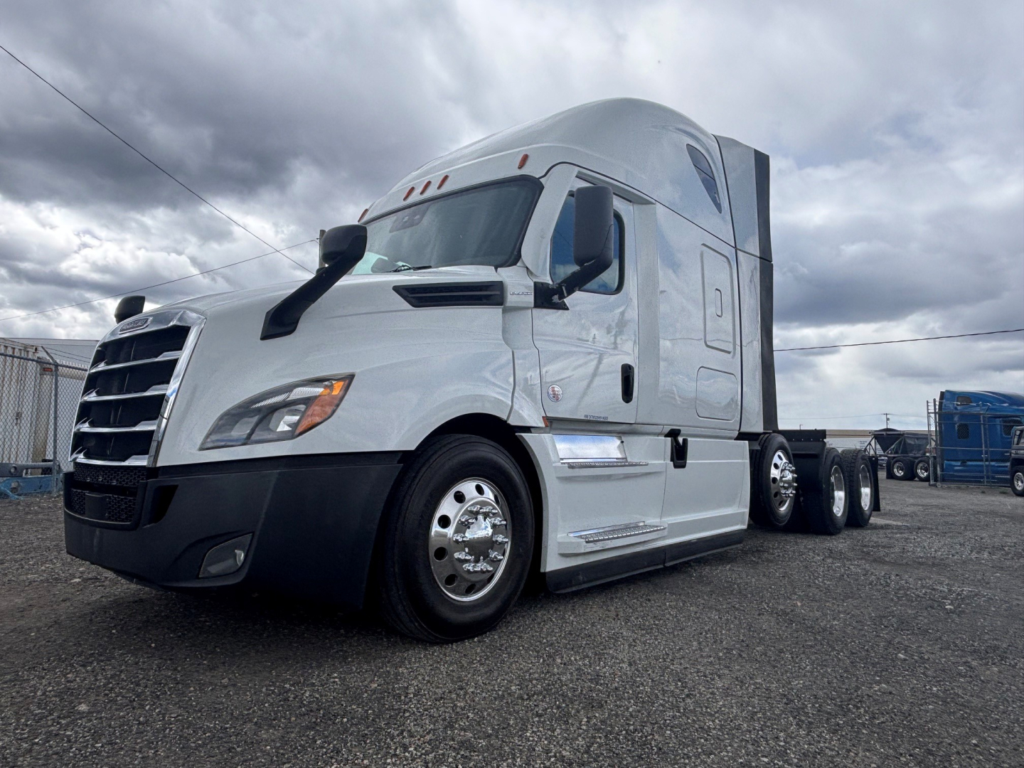 Freightliner truck in a lot; front-left view showing conventional sleeper cab, chrome wheels, and dual rear axles.