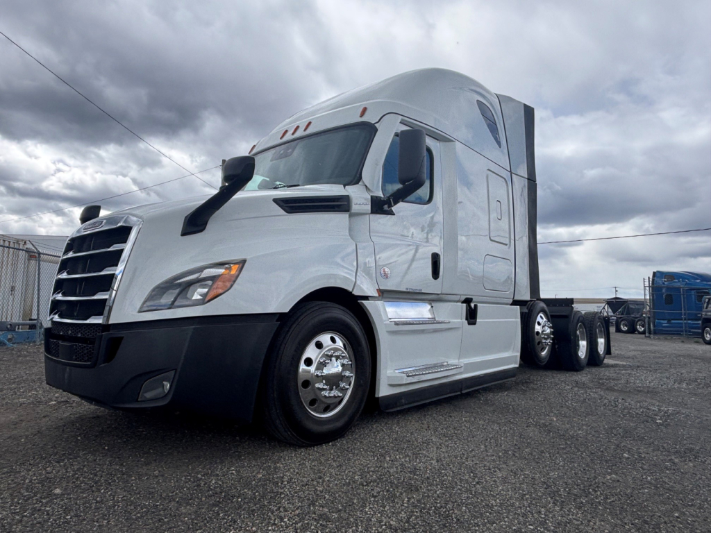 Freightliner truck in a lot; front-left view showing conventional sleeper cab, chrome wheels, and dual rear axles.