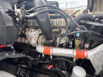 Truck engine bay showing intake hoses, coolant reservoir, and orange-capped hose in 2021 Freightliner CA-126 engine compartment.