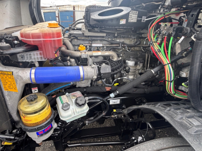 Truck engine bay showing coolant reservoir, braided hoses, and wiring harness in a Freightliner CA-126 engine compartment.