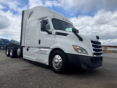 Freightliner highway tractor cab in white, front-right view showing sleeper cab, chrome wheels, and aerodynamic mirrors.