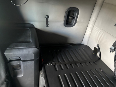 Cab interior showing sleeper area with ribbed rubber cargo floor, side wall with a small window/vent and a mounted latch; part of Freightliner CA-126 truck interior.