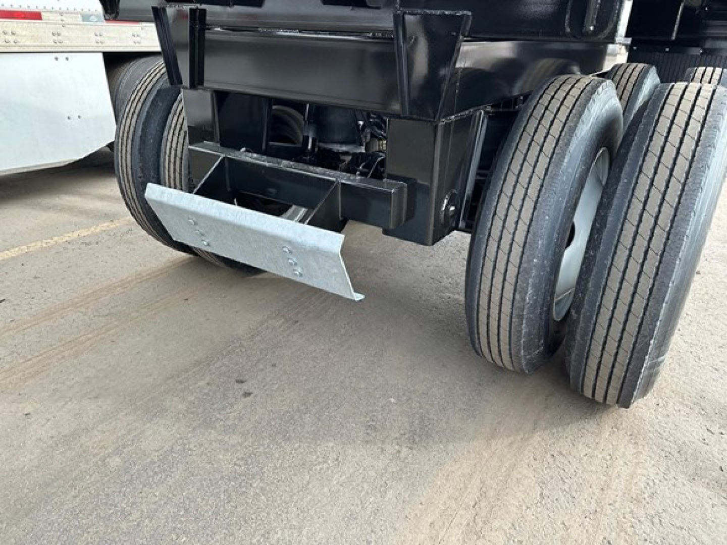 Trailer axle undercarriage showing dual rear axles and metal hitch; light weight bottom dump with electric ta in a yard.